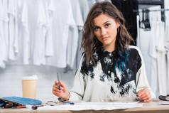 女时装设计师在餐桌上与咖啡杯在服装设计工作室工作