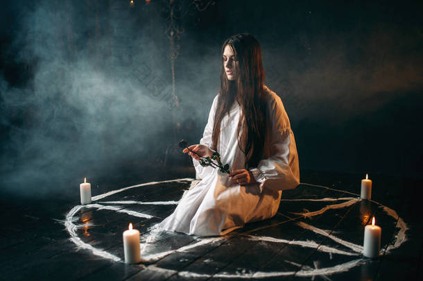 年轻女子手持燃烧的玫瑰手, 五角星圈与蜡烛和烟雾, 黑色魔术仪式, 神秘主义