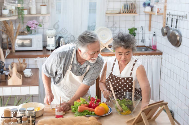 寻找新的食谱。亚洲一对老年<strong>夫妇</strong>在厨房里用数码平板电脑，闲暇时一起在家做饭.