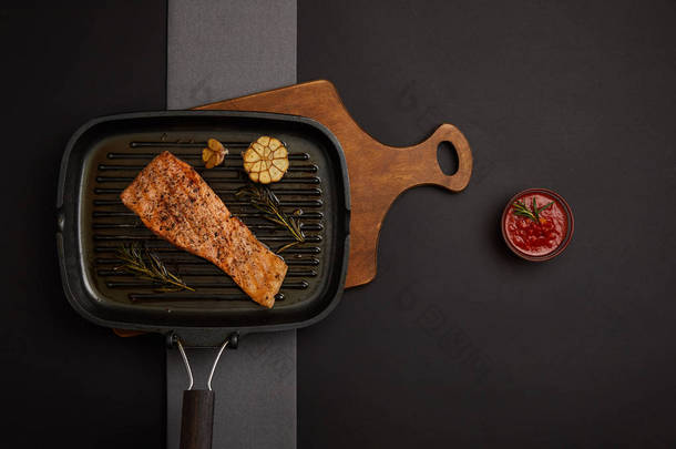 顶部视图的安排烤鲑鱼牛排在木制的切割板和酱油在黑色桌面上