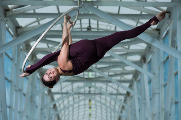一名空中体操运动员在悬挂在金属桁架上的空中吊环上进行分裂。马戏团的女演员在通风的戒指.