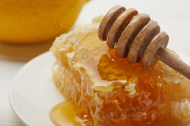 特写美味的蜂巢和木制蜂蜜滴管在盘子上