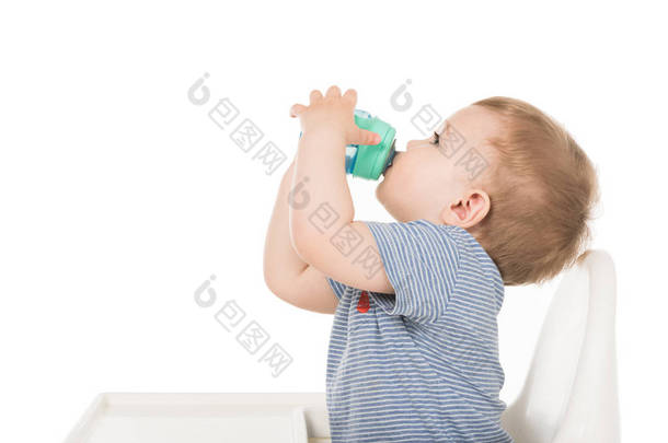 小男孩从婴儿杯饮水和坐在白色背景高脚隔离的侧面视图 