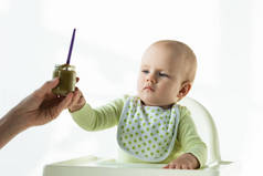母亲将婴儿营养罐给婴儿的选择重点放在白色背景的喂养椅上