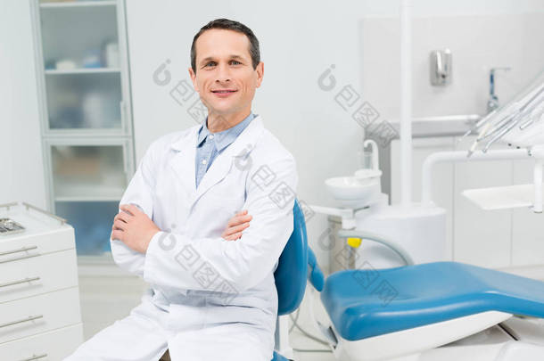 现代牙科诊所的微笑医生，双手交叉坐在那里