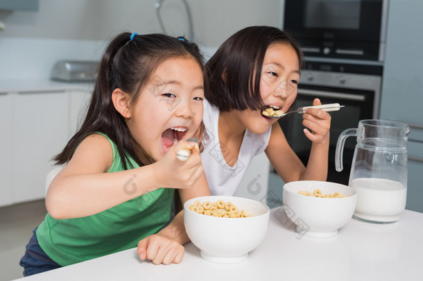 两个笑着年轻的女孩在厨房里吃谷类食品