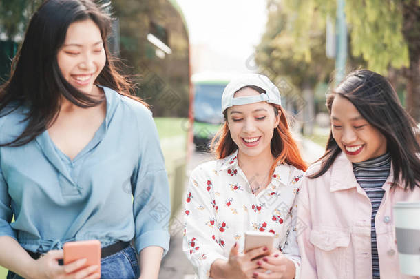 快乐的亚洲女孩们一边在城市里散步一边<strong>用手机</strong>观看- -年轻的少女们在玩新的社交媒体应<strong>用</strong>程序- -年轻的千年一代和技术概念