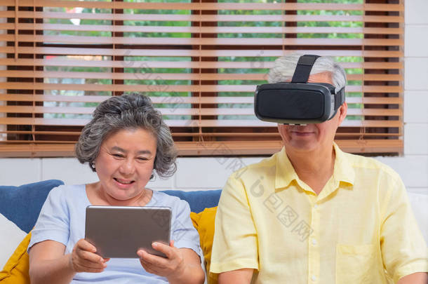 亚洲资深夫妇玩虚拟现实眼镜耳机和平板电脑<strong>观看</strong> vr <strong>视频</strong>, 并在家里客厅的沙发上一起玩。