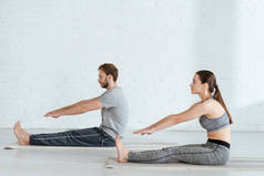 男子和妇女坐在前排弯曲姿势练习瑜伽的侧视图