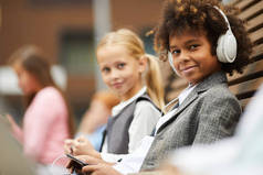 非洲学生头戴耳机，与坐在室外长椅上的女学生一起在手机上听录音