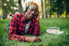 夏天公园里戴耳机躺在草地上的非洲学生