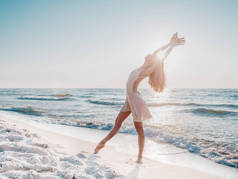 苗条美丽的芭蕾舞演员在白色礼服跳舞芭蕾在海上或海洋沙滩上晨光。艺术概念，自然之美