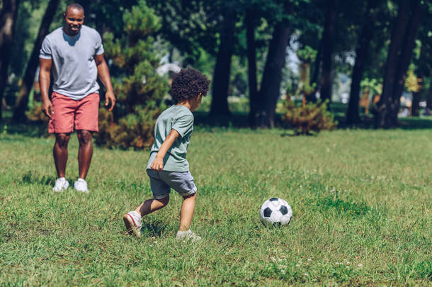 年轻的非洲裔美国父亲和可爱的儿子在公园踢足球