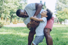 年轻的非洲裔美国父亲在公园里和可爱的儿子玩橄榄球