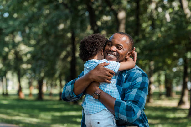 快乐的非洲裔美国父亲与闭上眼睛拥抱卷曲的儿子 