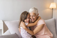 可爱的小女孩玩的乐趣与微笑的祖母拥抱躺在沙发上在一起, 快乐的奶奶和学龄前的孙子在沙发上放松, 孙女抱着拥抱在家里笑着