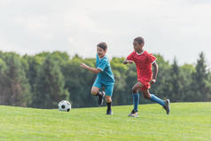 兴奋的多元文化的孩子在草地上踢足球 