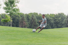 可爱的非洲美国男孩在绿草地上踢足球 