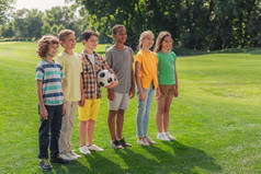 快乐的多元文化的孩子站在草地上与足球 