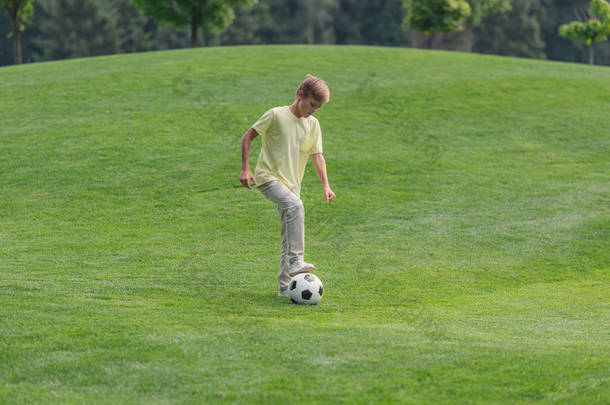 可爱的男孩在绿草地上踢足球 