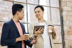 年轻的越南同事喝带走咖啡，讨论数字平板电脑上的信息