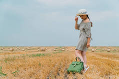 夏天的傍晚，一个戴着帽子，背着背包，背着袋子，站在麦田中央的漂亮姑娘