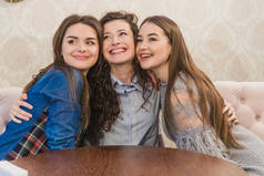 三个年轻女子坐在小咖啡馆里，靠在大窗户上，互相拥抱。美丽的年轻女孩喝咖啡。在白天的会议上.
