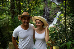 多元文化的夫妇在热带雨林中享受瀑布风光。年轻的混血夫妇在亚洲度假。彭尼布尔瀑布, 乌布, 巴厘岛.