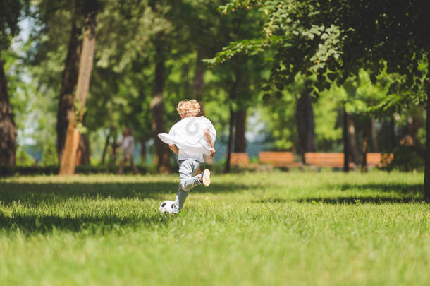 男孩在白天在公园里<strong>踢</strong>足球的后视图