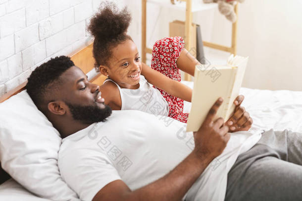 非洲男子读书给他的小女儿，躺在床上
