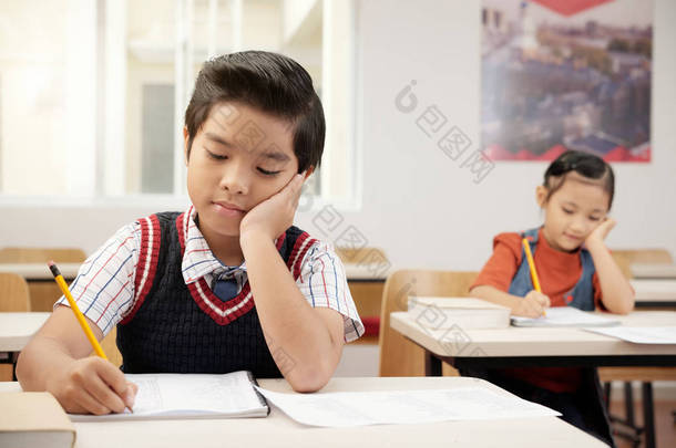 在教室里上课时，<strong>学生们</strong>坐在课桌旁，在笔记本上写字