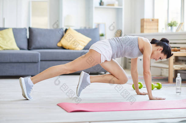 年轻女子，一条腿<strong>伸展</strong>，另一条腿弯成膝盖，在练习时趴在地板上