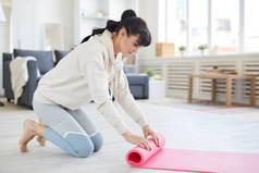 穿着活动服的年轻女子在客厅锻炼后穿上了粉色滚动垫子