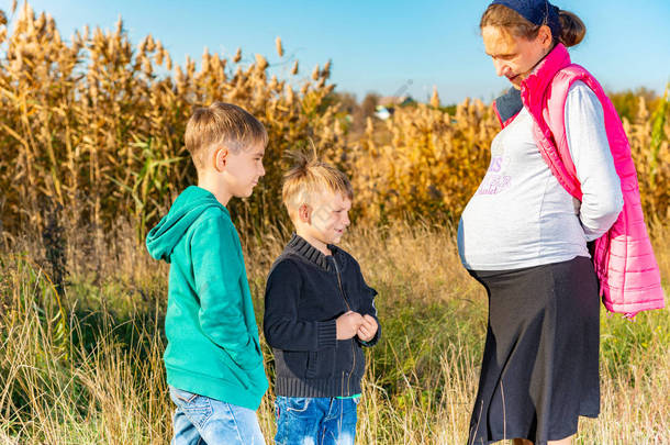 两个小兄弟正在看一个怀孕的母亲在公园散步的大肚子.