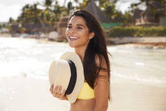 微笑的女孩与太阳帽子在海滩上, 看着了