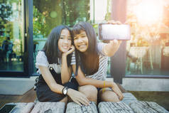 两个亚洲青少年显示智能手机屏幕的白色屏幕和牙齿笑脸幸福的情感