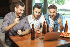 三个球迷喝啤酒, 看体育比赛的笔记本电脑在咖啡馆