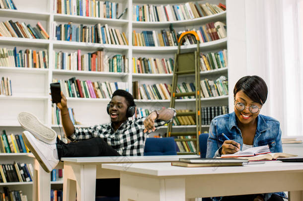 美丽的非洲裔美国学生在<strong>图书馆</strong>工作。女孩微笑着和笔记本电脑一起工作, 一边<strong>看书</strong>一边听音乐, 一边<strong>看书</strong>, 男孩跳舞.