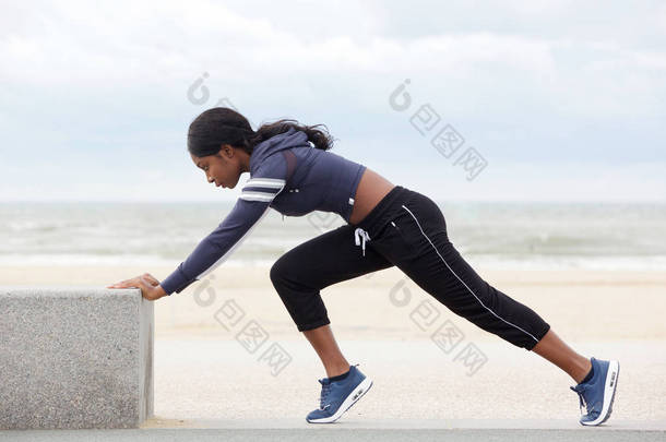 全身体侧肖像适合年轻的非洲裔美国妇女伸展<strong>肌肉</strong>在海滩上