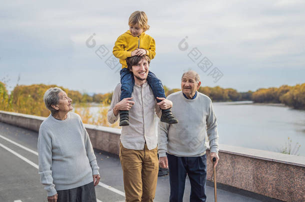 一对<strong>年迈</strong>的夫妇带着孙子和曾孙带着一条河走在公园里