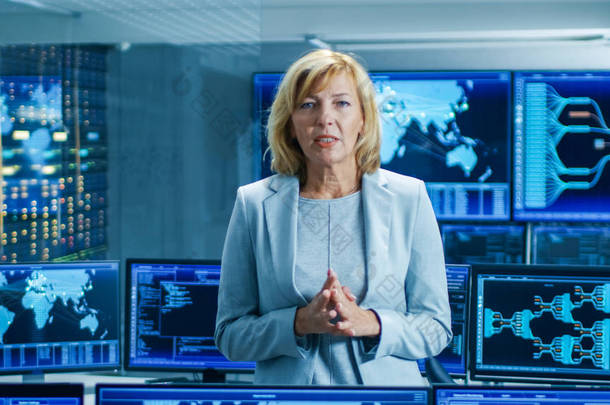 在系统控制室里, 女总工程师描述了她的项目在镜头中交谈。在后台显示交互式数据的多个屏幕.