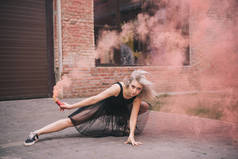美丽的年轻女舞蹈家在粉红色烟雾在街道上
