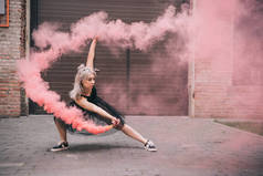 在城市街道粉红色烟雾跳舞的年轻妇女 