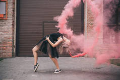 灵活的女孩跳舞在粉红色烟雾在城市街道  