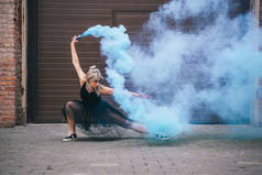 年轻的当代舞蹈家跳舞在蓝色烟雾在街道上 