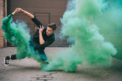 在绿色烟雾在街道上英俊的年轻男舞者