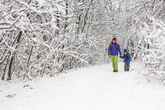 男孩和母亲一起走在积雪覆盖的森林小路上。寒假。有背包的孩子和他妈妈在一起玩.