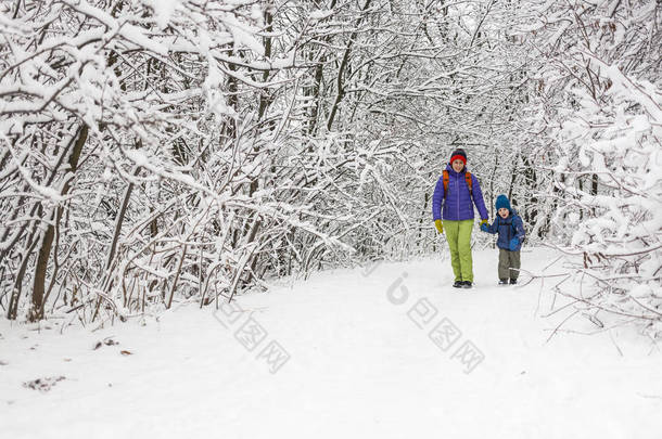 男孩和母亲一起走在积雪覆盖的森林小路上。寒假。有背包的孩子和他妈妈在一起玩.