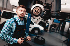 年轻的汽车修理工修理汽车轮毂在车库。专业制服。服务站的概念。自信的工程师盯着。细节修复。在车底下汽车诊断.