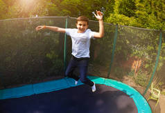 夏天青春期男孩在后院蹦床上跳得很高的画像